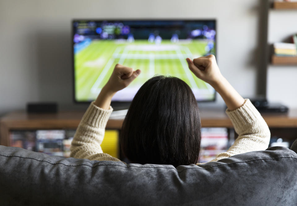 Young woman enthusiastically watching a tennis match on live sports streaming service on television, cheering with excitement.