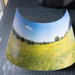 A large photo print that was shipped in a shipping tube and now has a very defined curvature, resting on a table.