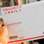 Close-up of a USPS delivery truck with the text "Sunday Delivery Services" highlighting Priority Mail Express and Amazon Packages