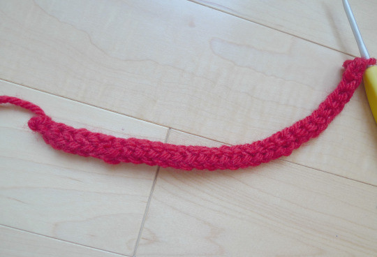 Close-up of the foundation single crochet row in bright red yarn, showing the beginning of the bow construction.