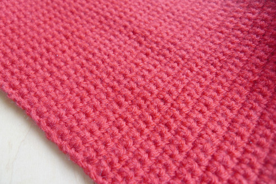 Completed rectangle panel of red crochet fabric, showing the width achieved after crocheting multiple rows.