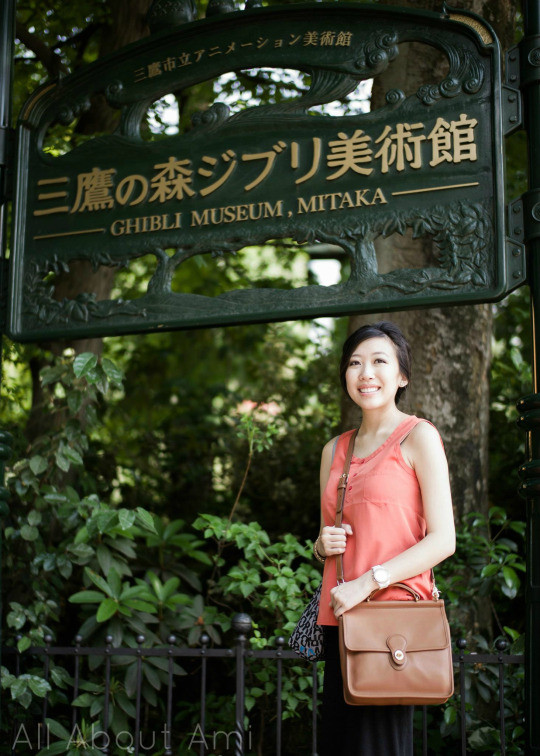 Pregnant woman in the rooftop garden of the Ghibli Museum, holding Totoro souvenirs and smiling amidst the garden's features.