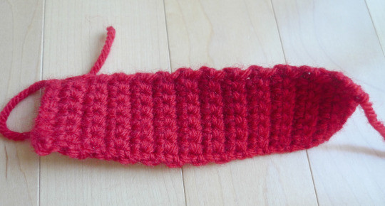 Narrow strip of red crochet fabric for the middle knot, shown with a yarn needle to prepare for assembly.