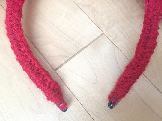 Headband being crocheted over with red yarn, demonstrating the process of covering the headband for the bow attachment.