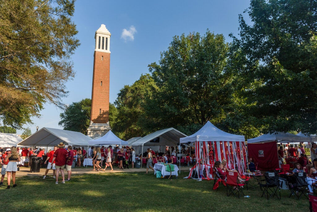 Fans tailgating on the Quad before an Alabama football game, setting up tents and grills, and enjoying the pre-game atmosphere.