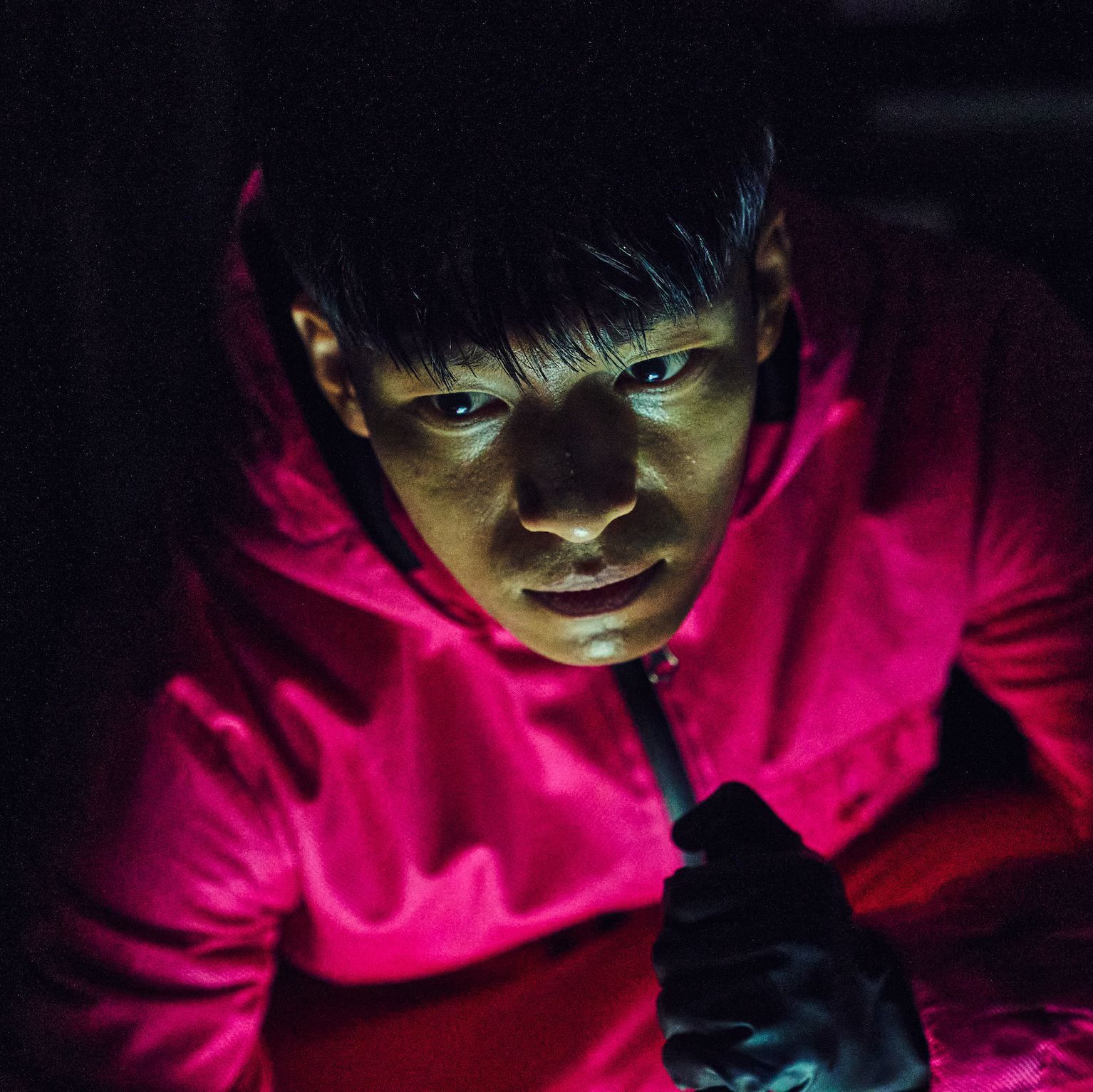 Wi Ha-joon as Hwang Jun-ho in a pink suit with a glow on his face in a still from squid game season 1