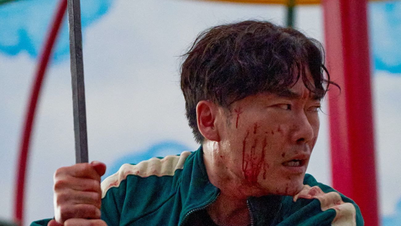 Yu Seong-ju as the doctor, or player 111, wielding a bar and with blood on his face in a still from squid game season 1