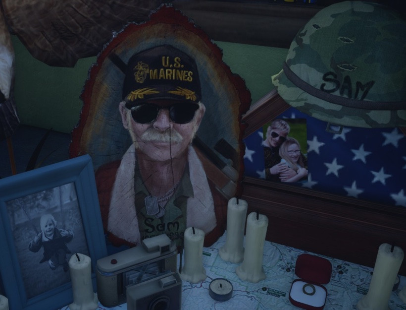 A memorial shrine featuring a painted portrait of an old white man with a mustache and sunglasses wearing a US Marines hat. Memorabilia include a camo helmet with the name Sam on it, a folded American flag, a picture of a child on a swing, a camera, a compass and a ring in a box.