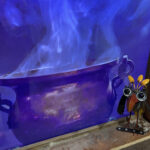 A video of a boiling cauldron with a small metal bird sitting beside it.