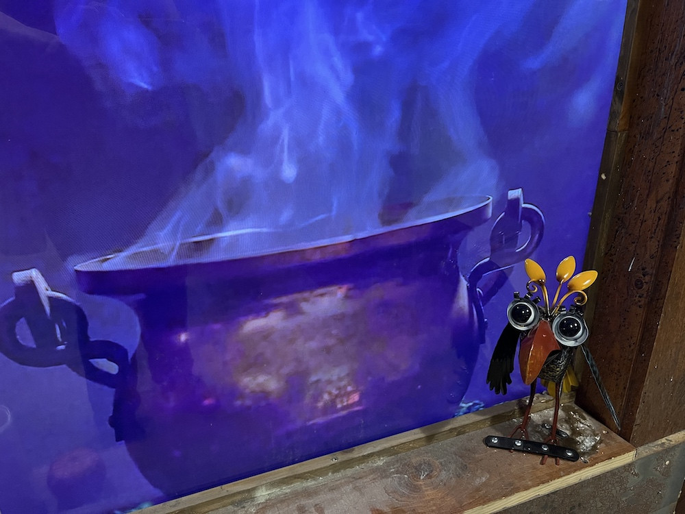 A video of a boiling cauldron with a small metal bird sitting beside it.