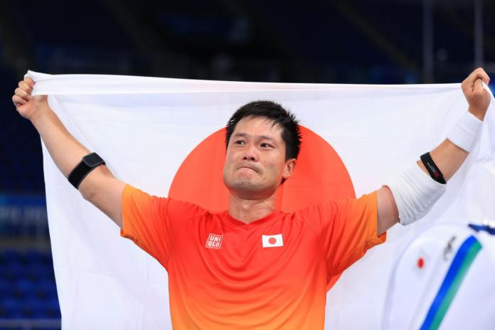 Wheelchair tennis player Shingo Kunieda holding the Japanese flag after winning the men's singles gold medal at the Tokyo 2020 Paralympics, showcasing his pride and accomplishment