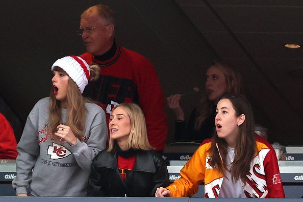 Taylor Swift cheering at the Patriots game with friends, wearing a beanie and skirt.