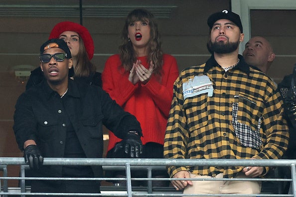 Taylor Swift watching the NFC Championship game with Cara Delevingne and Ross Travis, wearing a red sweater.
