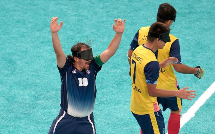 A man in a French football uniform and black eyeshade raises his arms in the air in celebration, with two players in Colombia football jerseys standing next to him, reflecting the competitive spirit of Argentina games