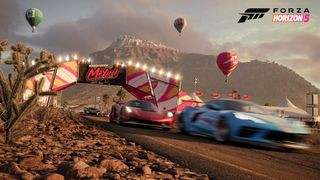 Forza Horizon 5 screenshot of a blue car speeding down a race track. A red car is close behind it, and hot air balloons can be seen floating in the sky in the background.