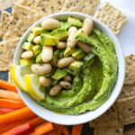 Vegan lemon avocado hummus dip with crackers and carrot sticks