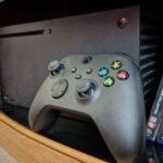 Xbox Series X lying horizontally with an Xbox Wireless controller leaning up against it in a TV unit