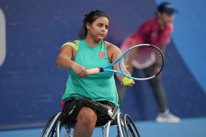 Female wheelchair tennis athlete Najwa Awane prepped to serve at the Tokyo 2020 Paralympic Games, demonstrating focus and athleticism