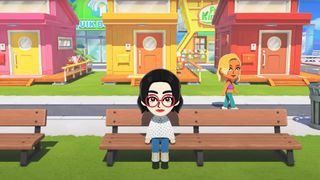 Screenshot from the reveal trailer of Tomodachi Life: Living the Dream, showing a female Mii sat on a bench as another female Mii walks on the street behind her