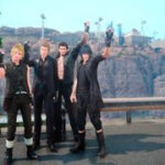 Final Fantasy 15 screenshot of four male characters standing on a roadside with rocky cliffs with builds atop them seen in the background.