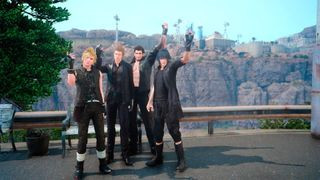 Final Fantasy 15 screenshot of four male characters standing on a roadside with rocky cliffs with builds atop them seen in the background.