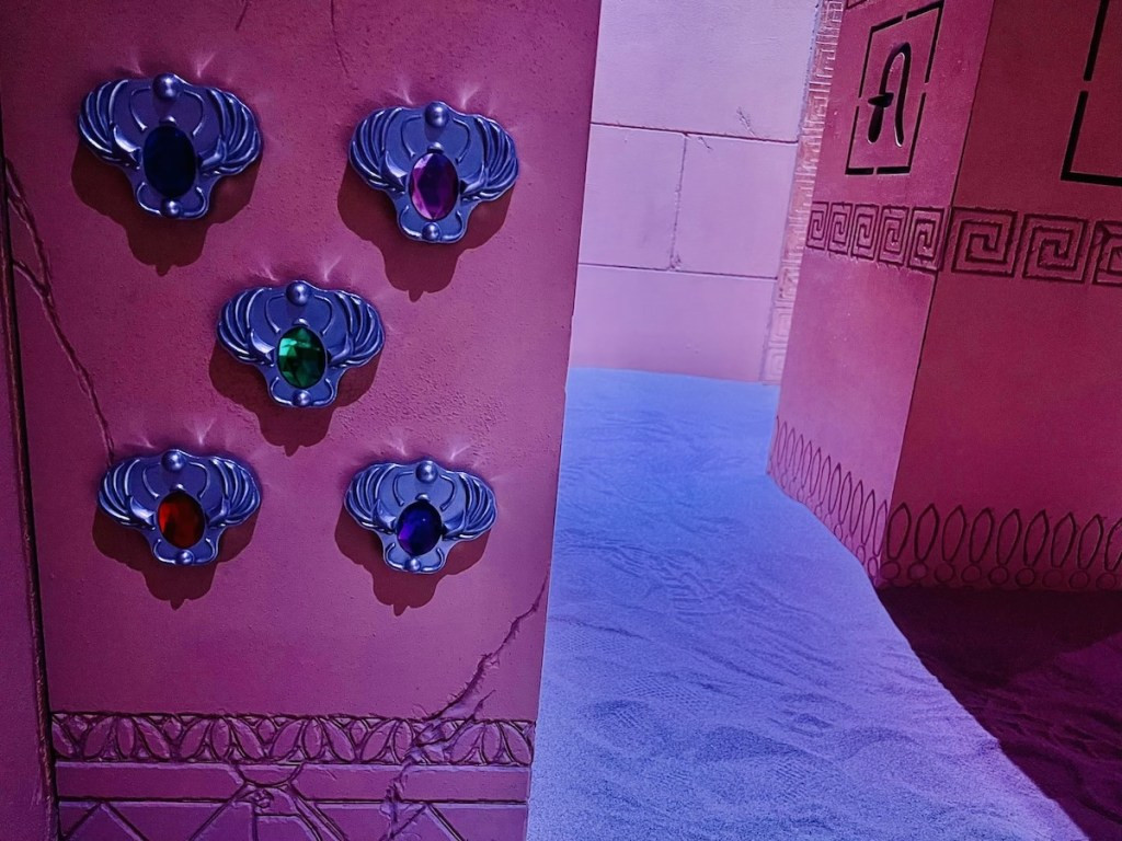 Five amulets, each with a different colored gem, mounted to a pillar, representing the puzzle elements of the escape room.