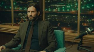 Alan Wake in live action, sitting on a green talk-show chair