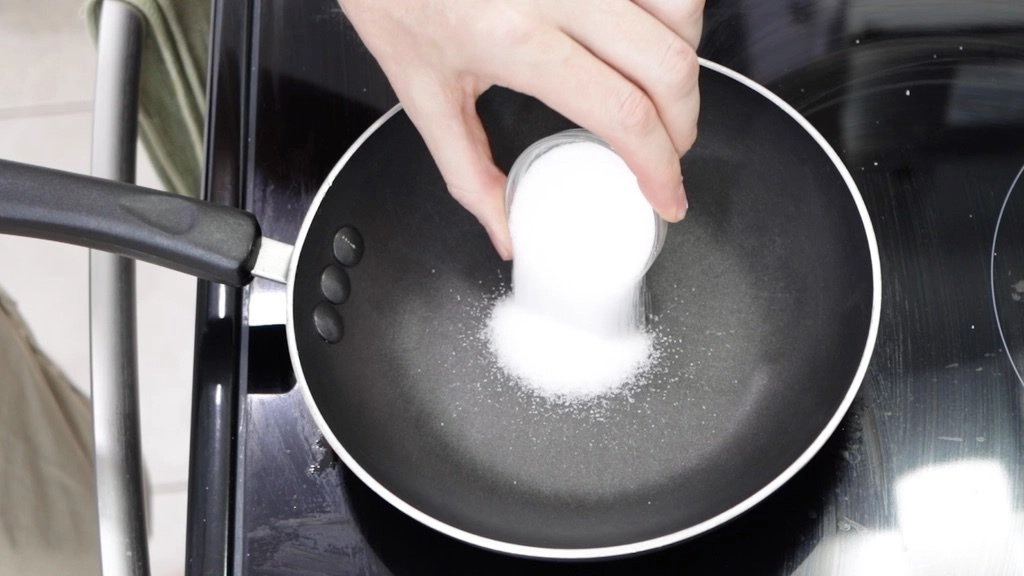 Pouring sugar onto a small skillet for Dalgona candy preparation.