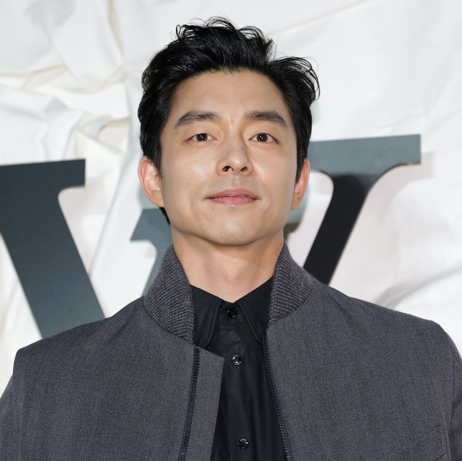 Gong Yoo, who plays the recruiter in squid game, posing in a grey jacket on a red carpet