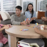 A family sitting at a table playing a card game, smiling and engaged.
