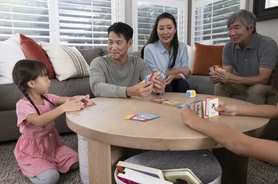 A family sitting at a table playing a card game, smiling and engaged.