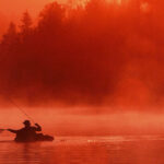 Woods Canyon Lake in Arizona with anglers fishing from the shore and boats amid pine trees and clear water.
