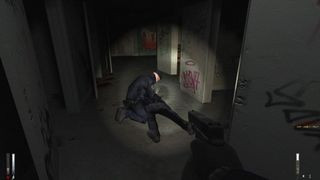 Cry of Fear screenshot showing a gun being held from a first-person viewpoint, with a flashlight shining on a man touching a body lying on the floor of a long dark corridor, emphasizing the game's tense and unnerving atmosphere