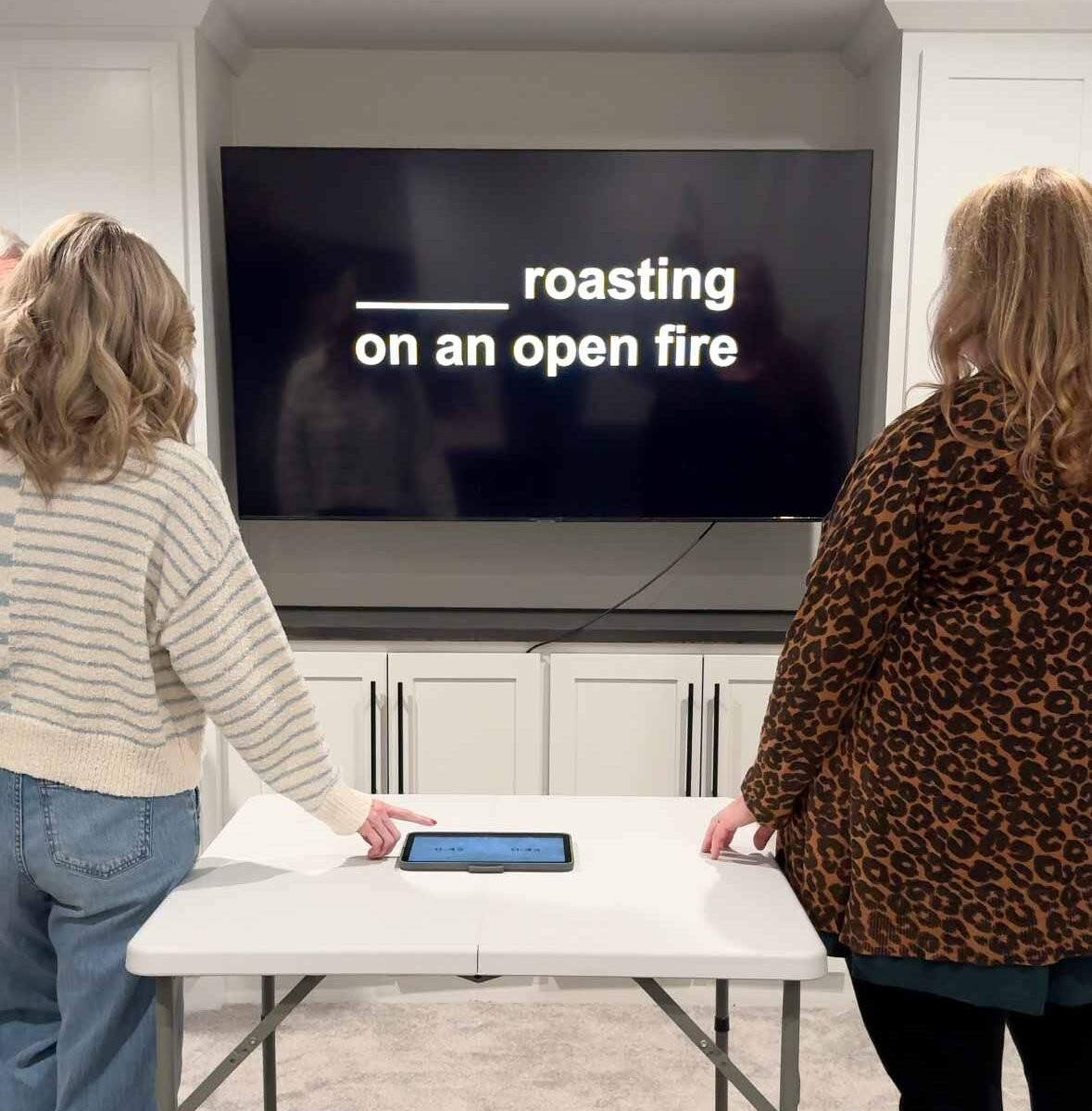 Two women standing ready to touch a button for answering questions on a TV