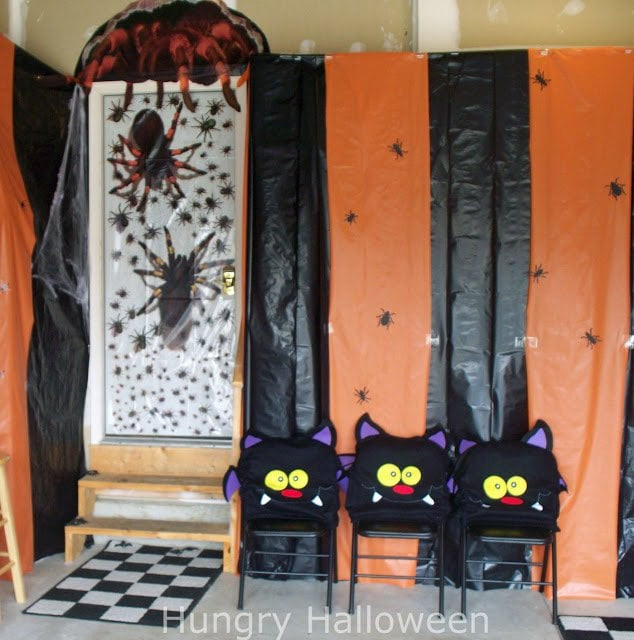our garage walls decorated with orange and black striped plastic, bug-themed door decoration, cut-out bugs, and bat chair covers.
