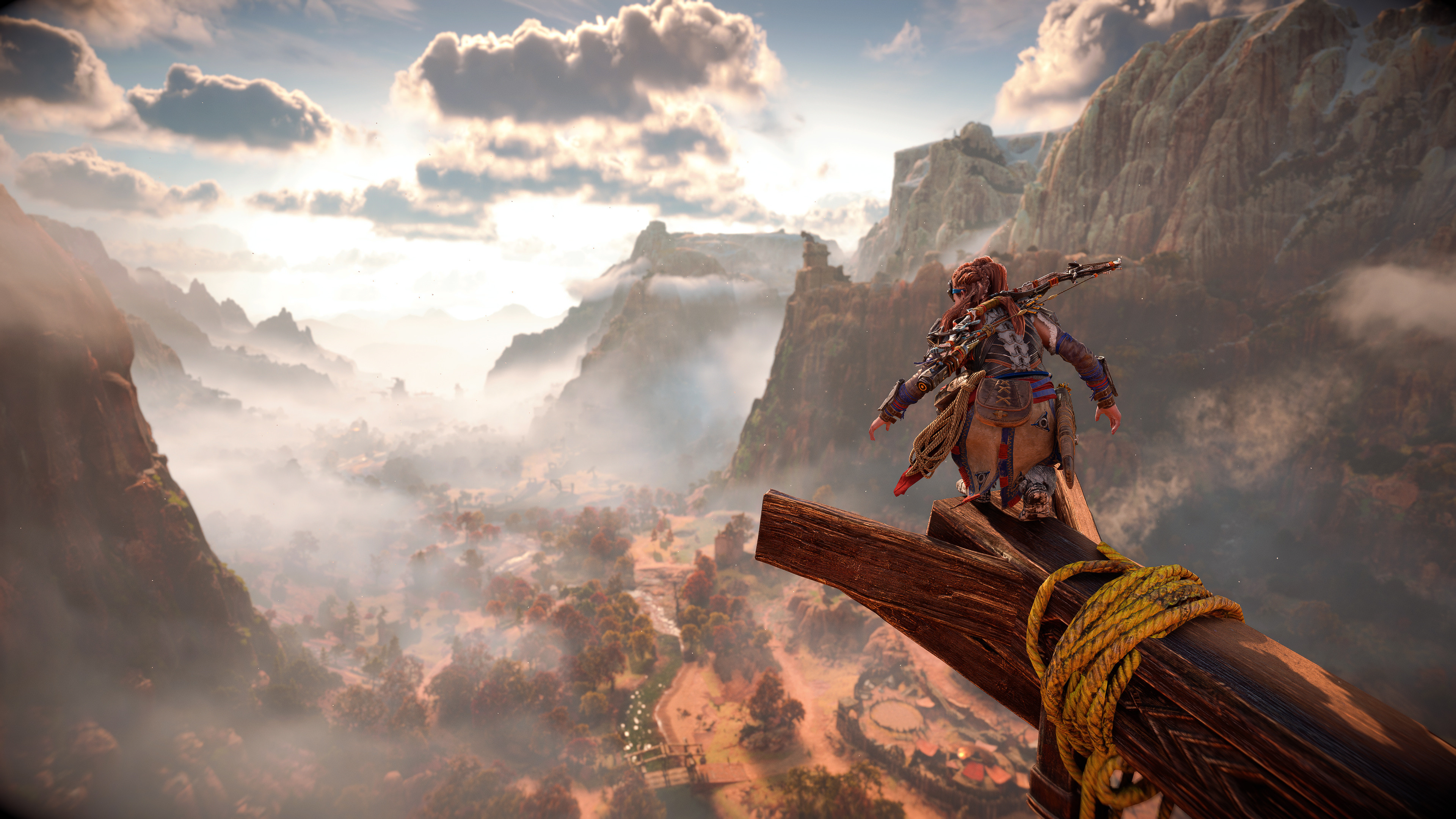 Aloy perched on a wood beam high above a misty river valley in Horizon Forbidden West on PS5. High-vantage point overlooking a misty landscape emphasizes the open-world of the game.