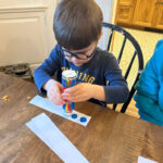 Child creating colorful patterns on paper strips for the Order Up Game