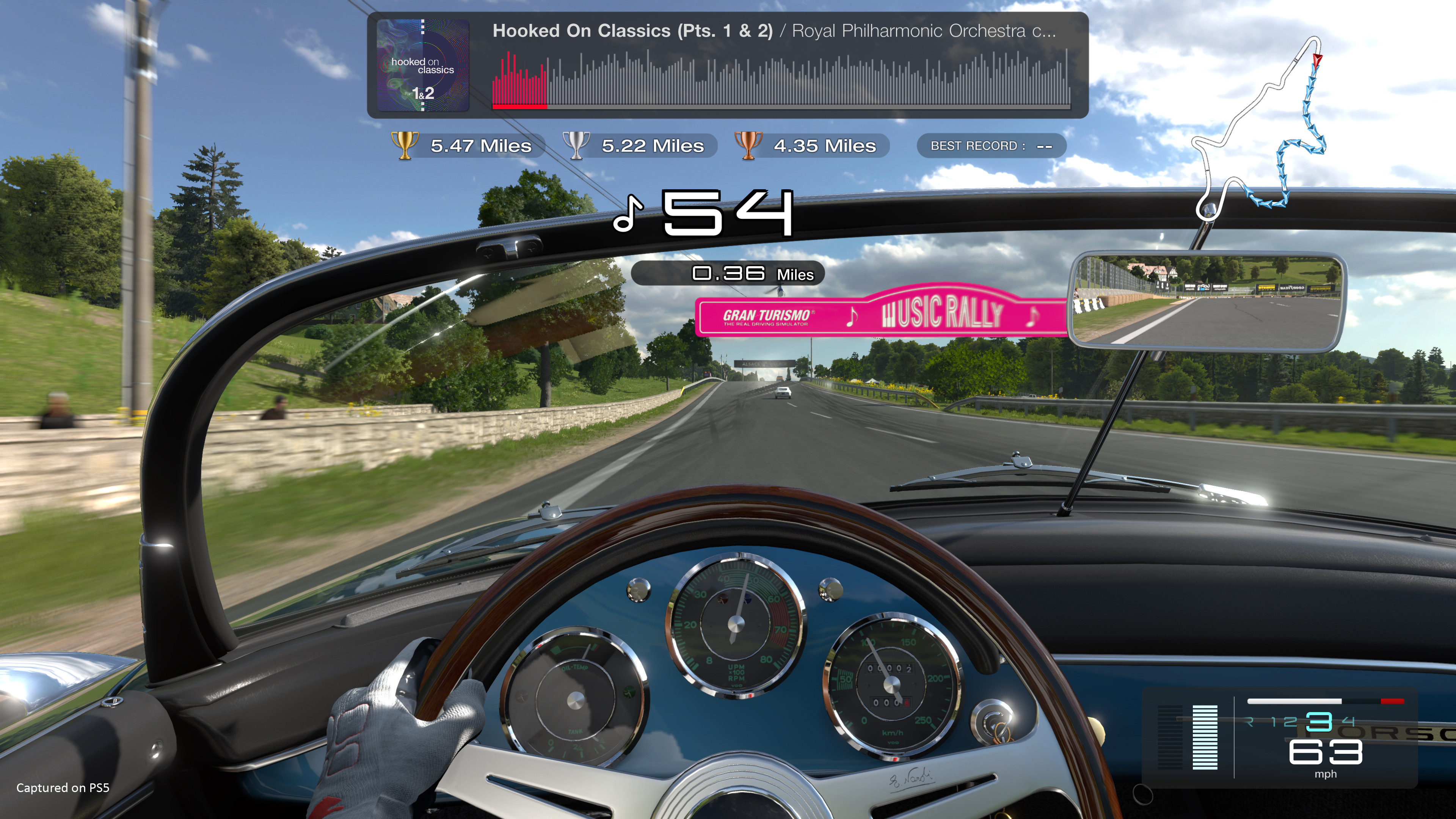 First person driver’s seat view of Gran Turismo 7’s Music Rally mode, showing interior of a vehicle. The image emphasizes realistic driving and music.