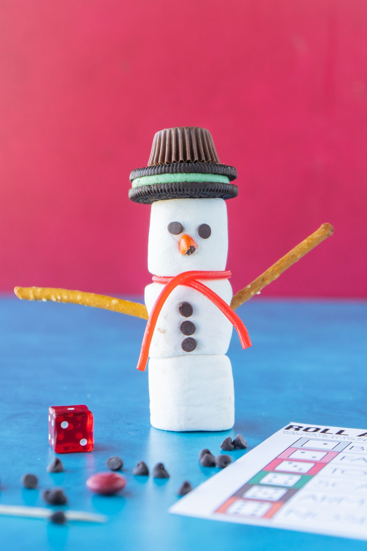 Marshmallow snowman standing next to a die